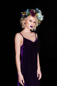 美丽的金发女孩摆在紫色的礼服和花花圈, 孤立的黑色