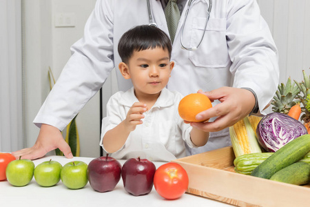 健康和营养的概念。孩子学习营养与医生选择吃新鲜的水果和蔬菜。年轻的亚洲男孩举行橙色