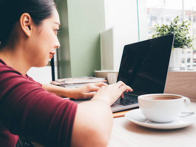 亚洲女人在咖啡馆里用笔记本电脑和一杯热咖啡