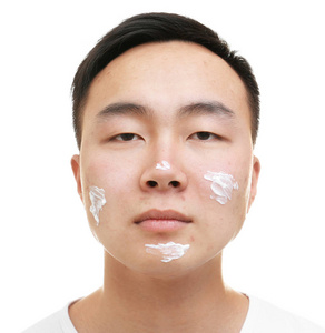 亚洲年轻男子问题皮肤应用到脸上，在白色背景上的奶油