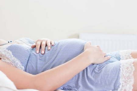 一个年轻的怀孕女人正坐在卧室里。孕妇放松