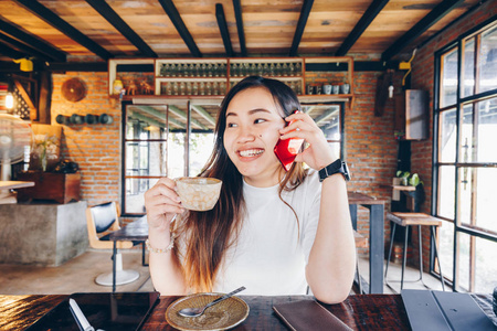 美丽的商业女性使用智能手机和平板咖啡杯在艺术咖啡馆