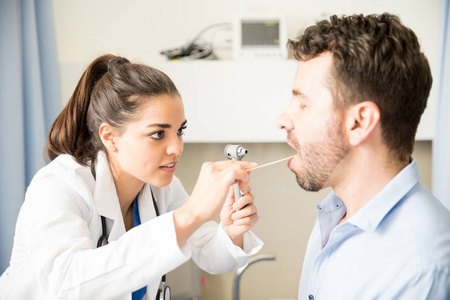 有吸引力的西班牙裔女医生用木棍和耳镜检查男性病人咽喉痛