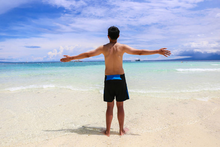快乐和开朗的穿泳装的男子举起手在沙滩上的水