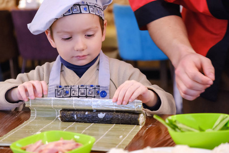 传统寿司卷的烹调。这个男孩打扮得像个厨师。