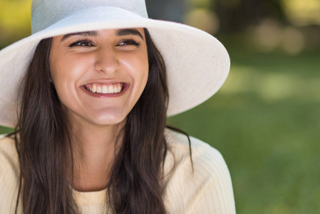 在公园里戴着一顶白色的帽子, 脸上露出了快乐微笑的年轻白种女人的肖像。生活方式和庆祝心情
