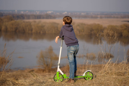 欧洲男孩用滑行车在河的高银行