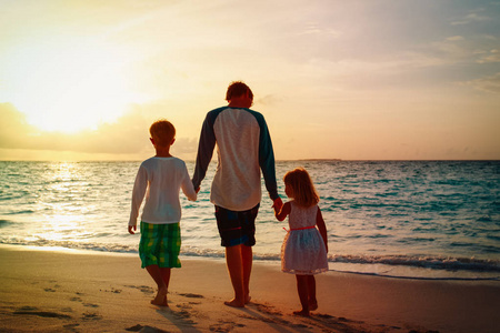 父亲与儿子和女儿在海滩漫步在日落