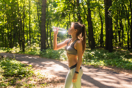 健身美丽的女人喝水和出汗后, 夏季炎热的一天在公园锻炼。女运动员下班后