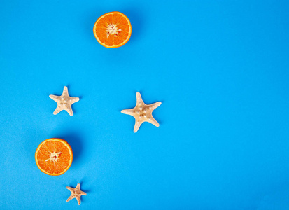 夏天的概念。橙色水果和海星在蓝色纸背景。平躺。复制空间