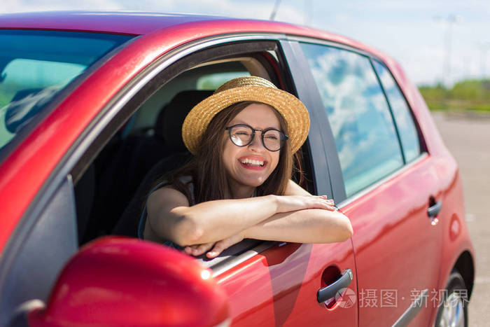 在车上的年轻女子.开车的女孩.微笑的年轻妇女坐在红色汽车