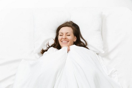 顶部视图的快乐黑发年轻女子躺在床上, 白色床单, 枕头, 毯子。微笑着漂亮的女性在房间里消磨时间。休息, 放松, 心情好的概念。