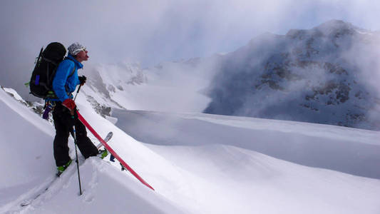 男性野外滑雪者在去山顶的路上休息一下, 在一个华丽的冬日里, 在小雪上表现得有点傻。