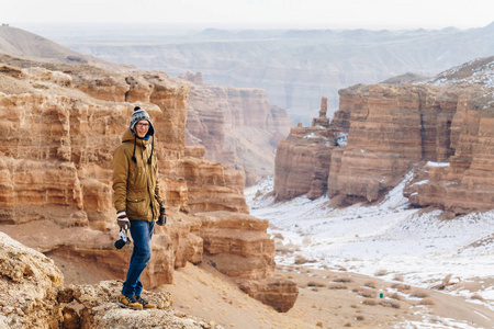 在哈萨克斯坦的 Charyn 峡谷, 一个带着照相机的快乐旅行者站在悬崖边上。
