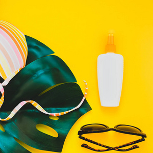 热带丛林棕榈龟背竹叶子, 太阳镜, 防晒霜空白瓶样机和妇女的泳装顶部在明亮的正方形黄色纸背景。暑期创意平躺概念模板