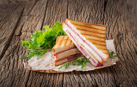 俱乐部三明治帕尼尼与火腿和奶酪在木质背景。野餐食品