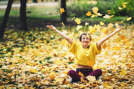 秋天的女孩坐在草地上, 高高兴兴地把黄叶。生活方式