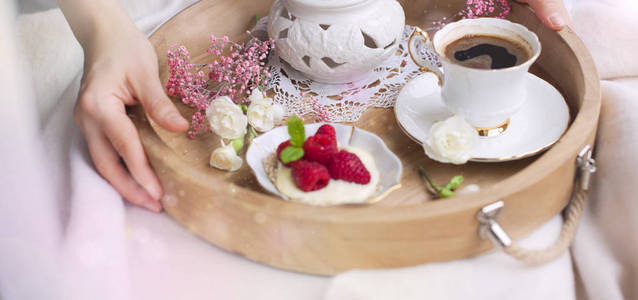 一个女人在床上喝咖啡。一个有早餐的木托盘。覆盆子浆果和花朵。浅色。浪漫。早上好。文本位置