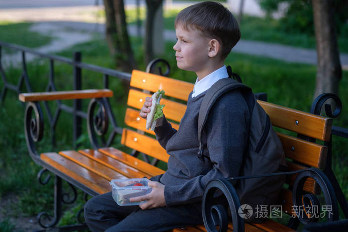 欧洲男孩在公园长椅上吃学校早餐