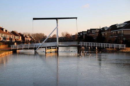 Nieuwerkerk 村中心的白色木质吊桥 Ijssel 在环形运河 Zuidplaspolder 与冰在清晨的阳光下