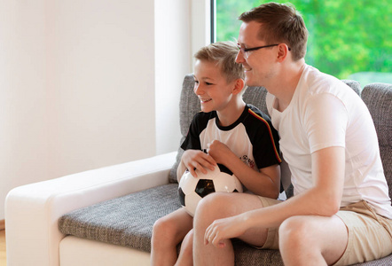 年轻的父亲和他的儿子看世界足球锦标赛与球在沙发上