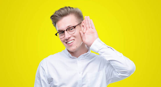 年轻英俊的金发男子微笑着用手在耳朵听谣言或八卦。耳聋概念