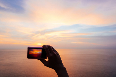 手持数码相机的女子手, 在平静的海面上拍照暮光的夕阳天空。摄影与视频户外自然拍摄