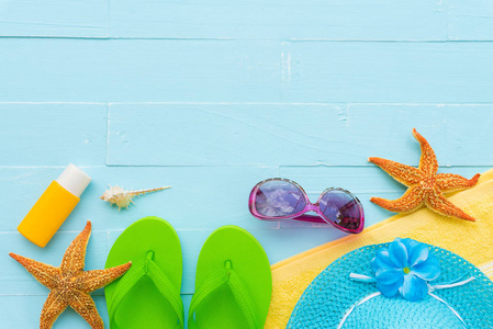 海滩配件包括太阳镜, 海星, 帽子海滩, 防晒霜, 五颜六色的翻转和贝壳在明亮的蓝色粉彩木背景为暑假和假日概念