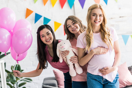 微笑的多元文化的朋友和怀孕妇女摆在婴儿聚会上的兔子玩具