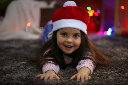 漂亮的小女孩在顶红色的帽子，躺在圣诞节装饰的房间