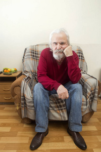 一个英俊的有病老头, 留着胡子, 长着白头发的胡子在养老院里独自坐在扶手椅上, 反映了过去的岁月。
