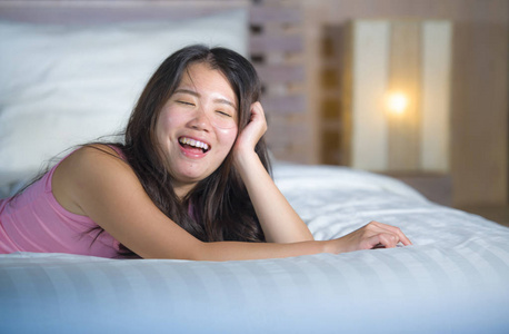 年轻美丽甜美的亚洲华人女子躺在床上嬉戏和舒适在她舒适的卧室里轻松愉快地微笑着欢快