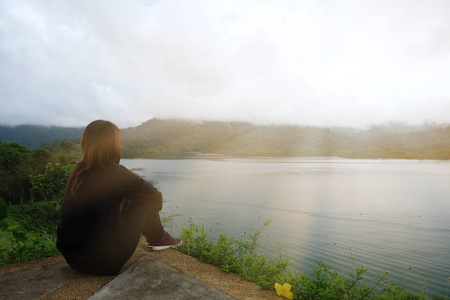 女人坐上独自悬崖。她前面有海和日落的时间背景。此图像的景观 度假与自然观