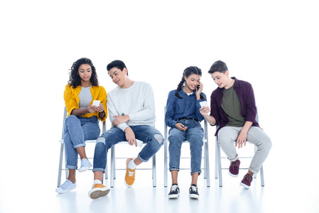 在白色隔离椅上使用智能手机的青少年学生组