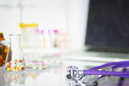 特写办公桌的医生办公室与一个听诊器在前景和一个瓶子与药片的背景下, 选择性的重点