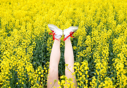 穿运动鞋的女性腿伸出花。腿起来。黄色油菜花的背景腿