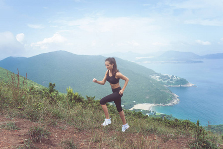 健身女运动员穿着黑色运动服做有氧运动，在山与励志海景中运行