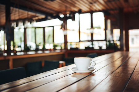 在木桌上的白色杯子里的热咖啡。咖啡厅里一张木桌上的一杯白咖啡。早上在咖啡馆里喝一杯陶瓷白咖啡