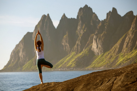 年轻女子正在练习瑜伽在挪威山之间