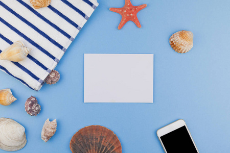 创意平躺的概念, 暑期旅游假期。海滩毛巾, 海贝壳, 海星和智能手机在柔和的蓝色背景上的顶级视图, 以最小样式复制空间, 文本模