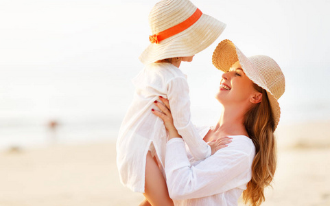 在海滩的幸福家庭。在日落时的母亲和孩子的女儿拥抱