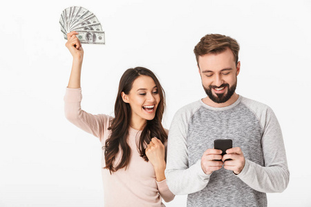 照片的幸福年轻的情侣站在白色背景下, 持有钱使用手机