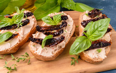 烤面包三明治 bruschetta 配奶油芝士干西红柿片和罗勒叶。木板上。美味佳肴