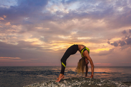 女人在日落做瑜伽。伸展运动女人在悬崖上