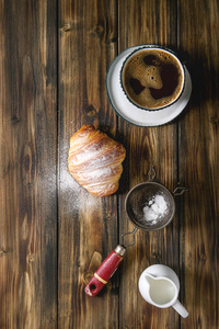 自制羊角面包, 配糖粉, 杯咖啡, 牛奶壶, 老式筛过木板背景。平躺, 空间