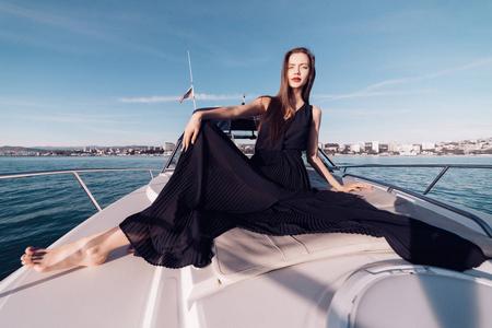 美丽的年轻女孩穿着时髦的黑色夏天的衣服, 她的白色游艇上休息, 享受在海上度假