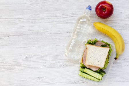 健康饭盒配有三明治水果和瓶装水, 白色木质背景, 平躺。从上面。复制空间