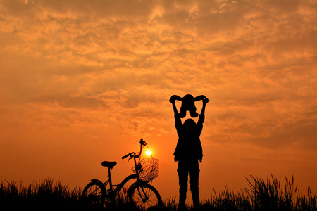 女孩脚踏车的草田天空日落时的剪影
