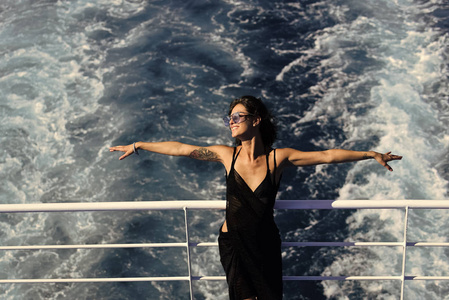 在渡轮上休息。迷人的女孩感到自由和享受暑假。自由概念。的女士站在甲板上邮轮与海浪的背景。妇女在礼服旅行在巡航