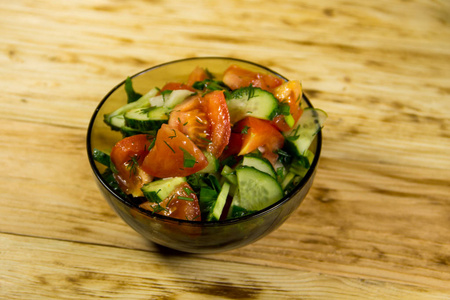 番茄，黄瓜，洋葱，欧芹和莳萝在木制的桌子上的玻璃碗中的新鲜沙拉